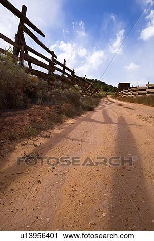 Stock Image - View of traditional old wooden fence and red sandy road, sunny afternoon with blue sky, Pleasant Valley, Utah. Fotosearch