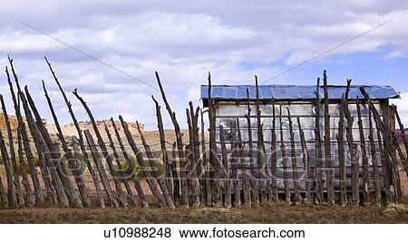Stock Photo - Wooden fence around corral: inside, a wooden plank shed, white with blue roof, set against blue sky and white puffy clouds, Utah. Fotosearch