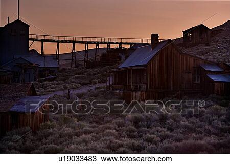 Stock Image - Wooden mining buildings, housing and bridge at dawn, with wild sage, Bodie pioneer village, California. Fotosearch