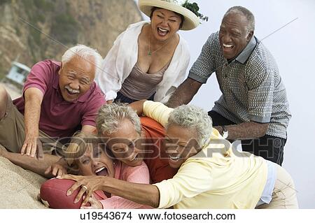 Picture - Adult friends playing American football on beach. Fotosearch