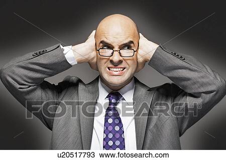Stock Image - Bald businessman holding hand over ears, looking sideways, making a face. Fotosearch