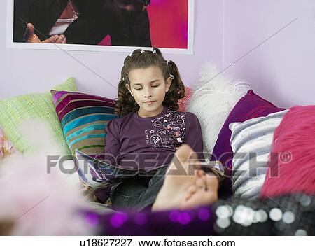 Barefoot Young Girl Reading Magazine, reclining on bed with many pillows View Large Photo Image Stock Photo - Barefoot Young Girl Reading Magazine, reclining on bed with many pillows. Fotosearch