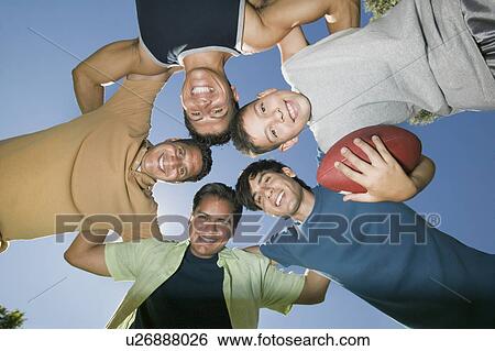 Stock Photograph - Boy (13-15) holding football, with brothers and father in huddle, view from below.. Fotosearch
