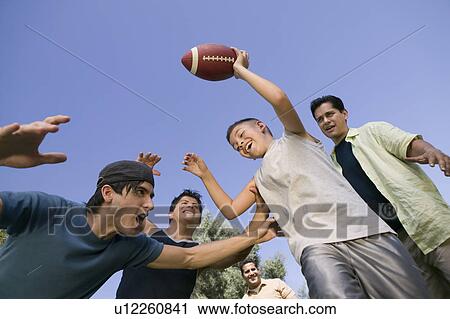 Stock Image - Boy (13-15) playing football with group of young men, low angle view.. Fotosearch