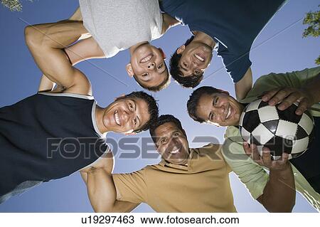 Stock Image - Boy (13-15) with brothers and father in huddle, view from below.. Fotosearch