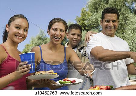 Stock Image - Boy (13-15) with family, gathered around outdoor grill.. Fotosearch
