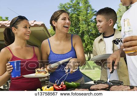 Stock Photo - Boy (13-15) with family, gathered around grill at picnic.. Fotosearch