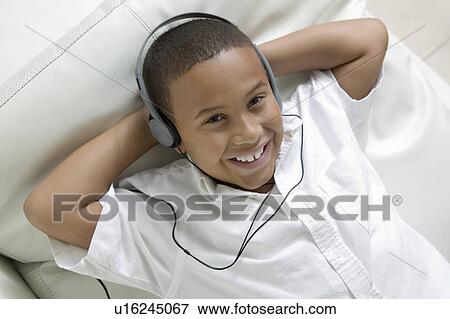 Stock Photo - Boy lying on sofa Listening to Music on Headphones, portrait, overhead view. Fotosearch