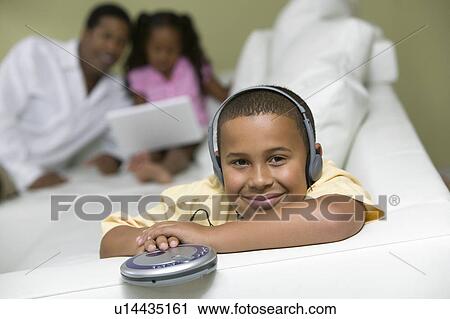 Stock Image - Boy on sofa Listening to portable CD player, portrait. Fotosearch