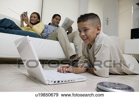 Boy Using Laptop on Floor in living room, mother and father on sofa, ground view View Large Photo Image Stock Photo - Boy Using Laptop on Floor in living room, mother and father on sofa, ground view. Fotosearch