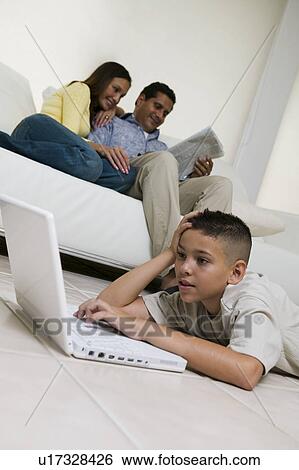 Boy Using Laptop on Floor in living room, mother and father on sofa, ground view View Large Photo Image Stock Photograph - Boy Using Laptop on Floor in living room, mother and father on sofa, ground view. Fotosearch