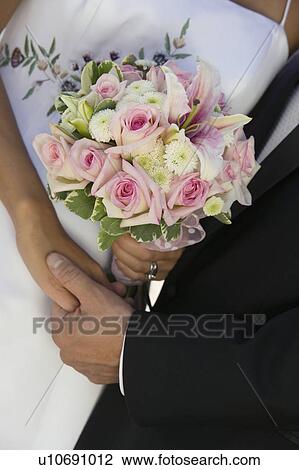 Stock Image - Bride and Groom holding hands and bouquet, (close-up). Fotosearch