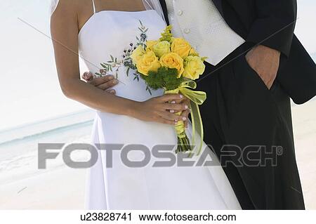 Stock Image - Bride and Groom with bouquet on beach, (close-up). Fotosearch