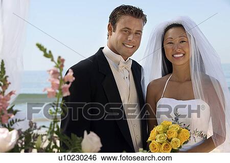 Stock Photograph - Bride and Groom with flowers at ocean, (portrait). Fotosearch