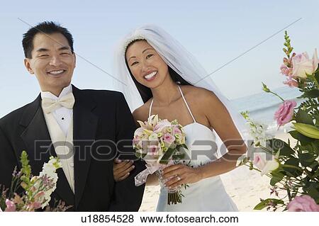 Stock Photo - Bride and Groom with flowers on beach, (portrait). Fotosearch