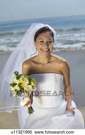 Stock Photography - Bride with bouquet on beach, smiling, (portrait). Fotosearch
