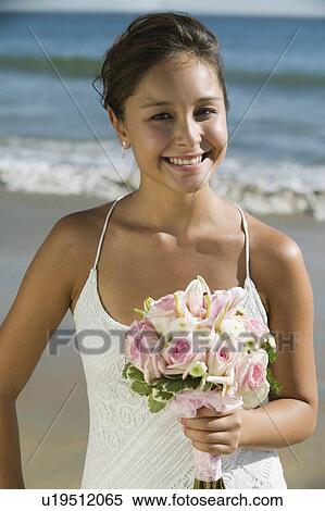 Stock Photography - Bride with bouquet on beach, smiling, (portrait). Fotosearch