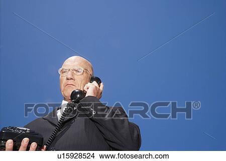 Picture - Busieness man using phone standing against sky, low angle view. Fotosearch