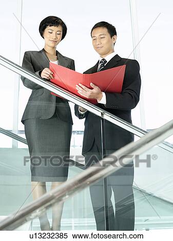 Stock Photography - Business colleagues reviewing documents while standing on stairs. Fotosearch