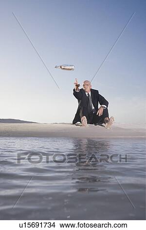 Business man sitting on beach, throwing message in bottle into sea, low angle view View Large Photo Image Picture - Business man sitting on beach, throwing message in bottle into sea, low angle view. Fotosearch