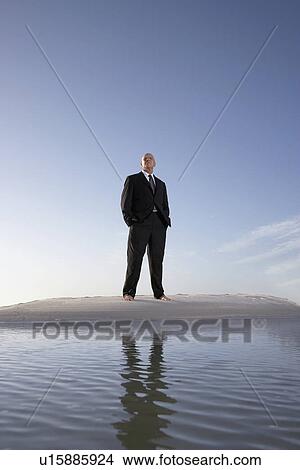 Picture - Business man standing on beach, portrait, low angle view. Fotosearch
