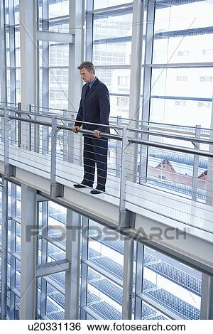 Stock Photograph - Businessman by railing in modern building. Fotosearch