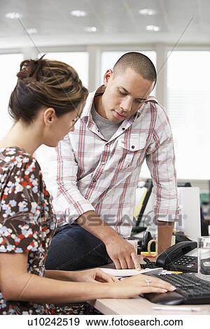 Stock Photo - Businessman sitting on desk pointing out something to Co-Worker. Fotosearch