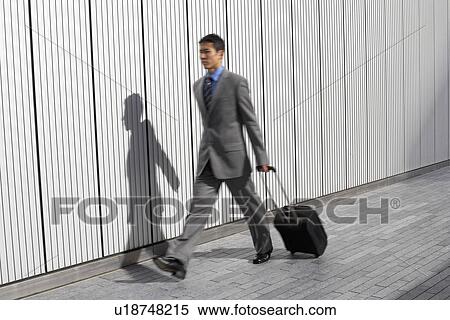 Businessman walking outdoors, pulling suitcase behind him View Large Photo Image Stock Photography - Businessman walking outdoors, pulling suitcase behind him. Fotosearch