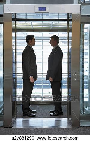 Businessmen standing face to face in elevator View Large Photo Image Stock Image - Businessmen standing face to face in elevator. Fotosearch