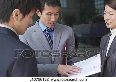 Businesspeople standing outside, looking over documents View Large Photo Image Stock Image - Businesspeople standing outside, looking over documents. Fotosearch