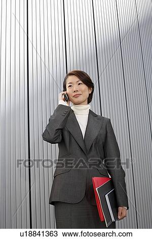 Stock Image - Businesswoman holding paperwork, using Cell Phone. Fotosearch