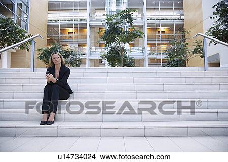 Picture - Businesswoman sitting on steps outside office. Fotosearch