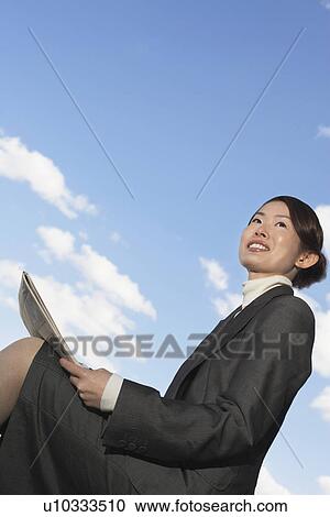 Businesswoman sitting outdoors, reading newspaper, low angle view View Large Photo Image Stock Image - Businesswoman sitting outdoors, reading newspaper, low angle view. Fotosearch