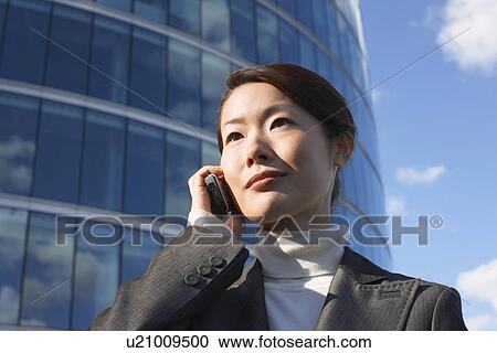 Stock Image - Businesswoman standing outside office building, Using Cell Phone, close-up. Fotosearch