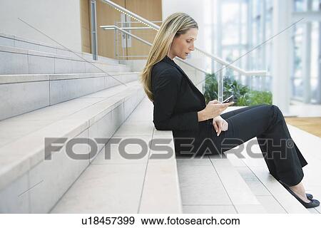Stock Photo - Businesswoman text messaging on steps outside office. Fotosearch