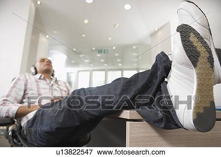 Casually dressed Businessman reclining with feet on desk, Listening to Music With Headphones View Large Photo Image Stock Photo - Casually dressed Businessman reclining with feet on desk, Listening to Music With Headphones. Fotosearch