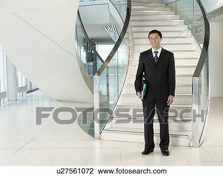 Confident Businessman, holding folder, standing in front of stairs View Large Photo Image Stock Image - Confident Businessman, holding folder, standing in front of stairs. Fotosearch