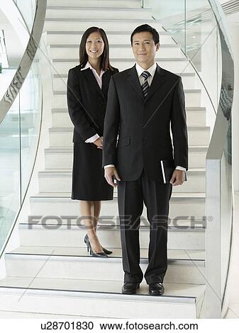 Stock Image - Confident Businesspeople standing on staircase. Fotosearch