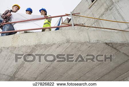 Stock Image - Construction team examining building plans on site. Fotosearch