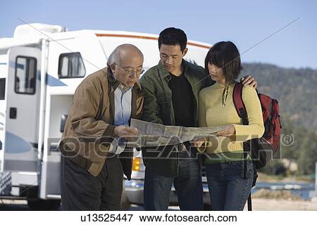 Stock Photo - Couple and senior father reading map outside RV. Fotosearch
