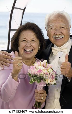 Stock Photo - Couple at wedding giving thumbs-up, smiling, (portrait). Fotosearch