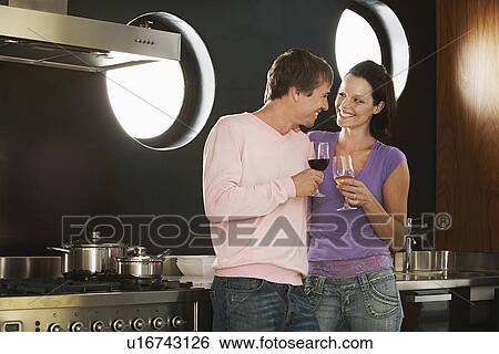 Stock Photograph - Couple drinking wine in modern kitchen, half length. Fotosearch