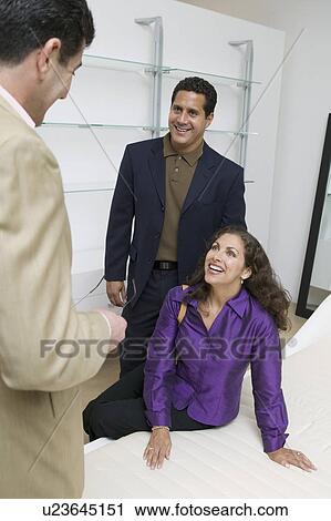Stock Image - Couple Examining Mattress With Salesman in furniture store. Fotosearch