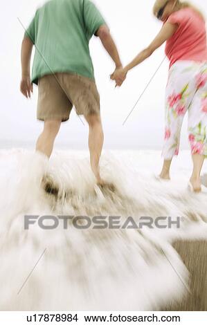 Picture - Couple holding hands, walking in surf. Fotosearch