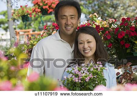 Stock Photo - Couple holding plants in plant nursery, portrait. Fotosearch