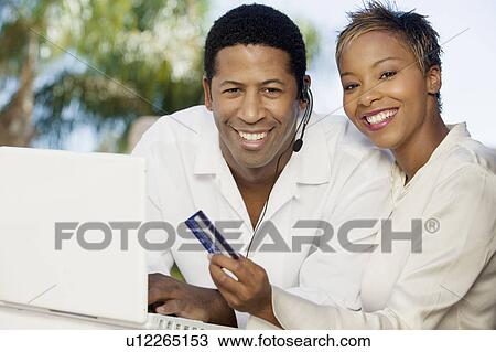 Stock Image - Couple on patio making online credit card purchase, portrait. Fotosearch
