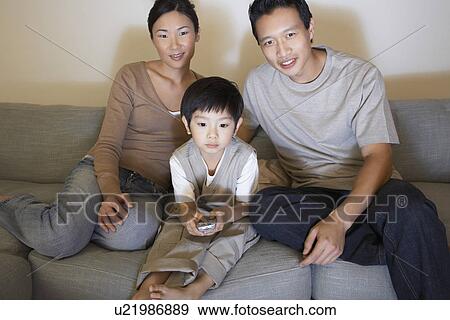 Stock Photo - Couple sitting on sofa, Watching Television while son is using remote control. Fotosearch