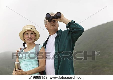 Stock Image - Couple using binoculars in countryside. Fotosearch