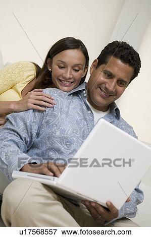 Couple Using Laptop Together on sofa in living room View Large Photo Image Stock Photo - Couple Using Laptop Together on sofa in living room. Fotosearch