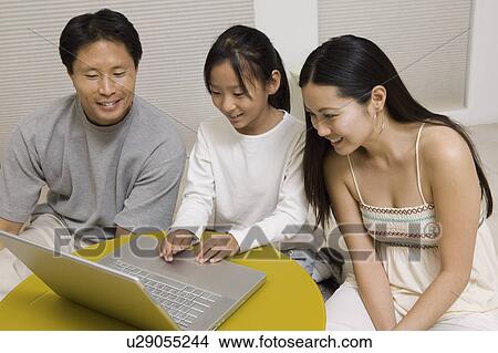 Picture - Daughter using laptop with mother and father in living room. Fotosearch